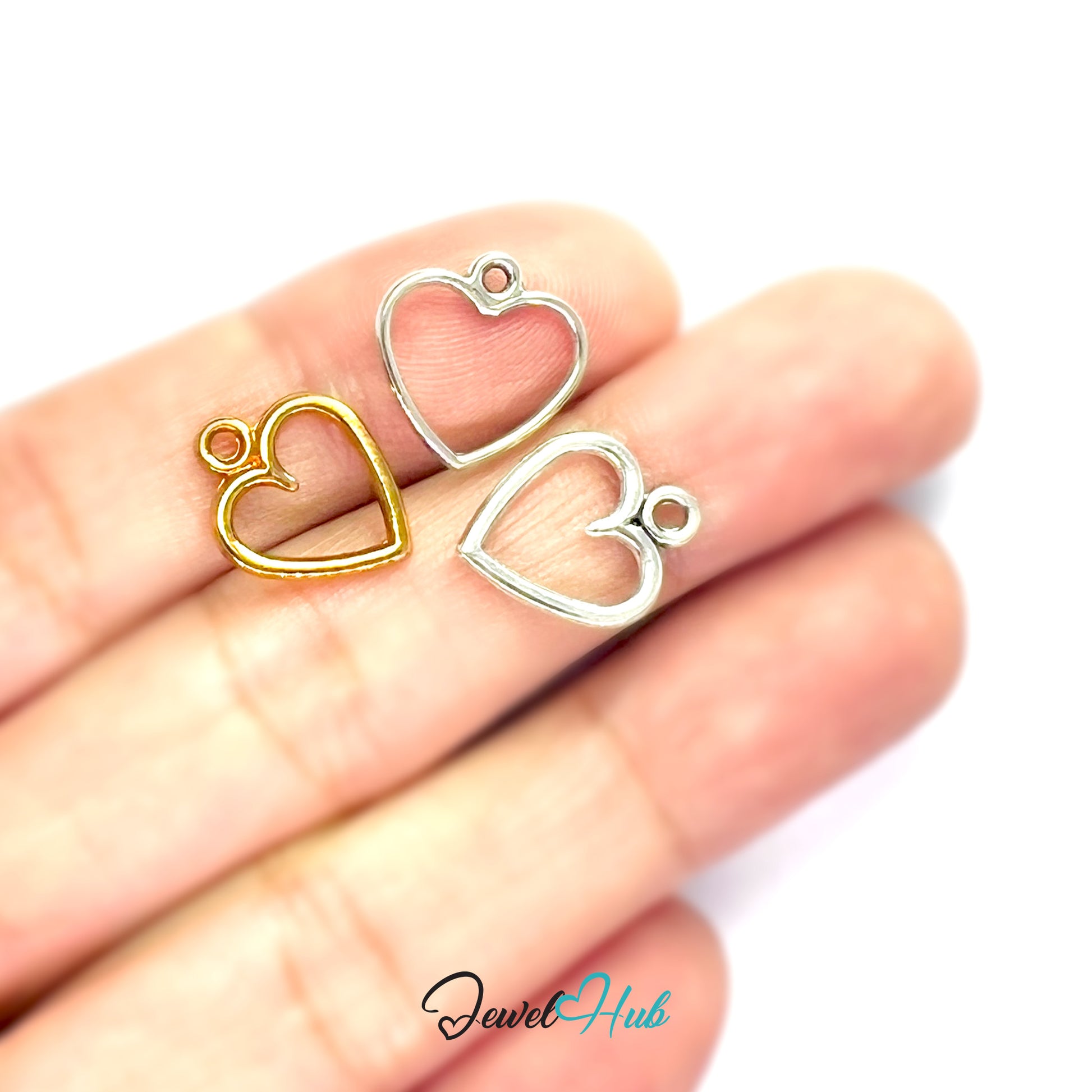 Two heart-shaped metal charms, one gold and one silver, held between fingers on a white background with 'Jewel Hub' branding.