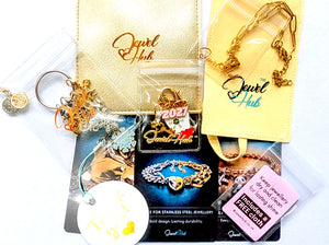 JewelHub Event Gift Bag contents laid flat: stainless steel paperclip chain bracelet, charm keyring with clip-on charms, gold and cream zip pouches, three material care cards, a Thank you tag and a free mini jewellery cloth