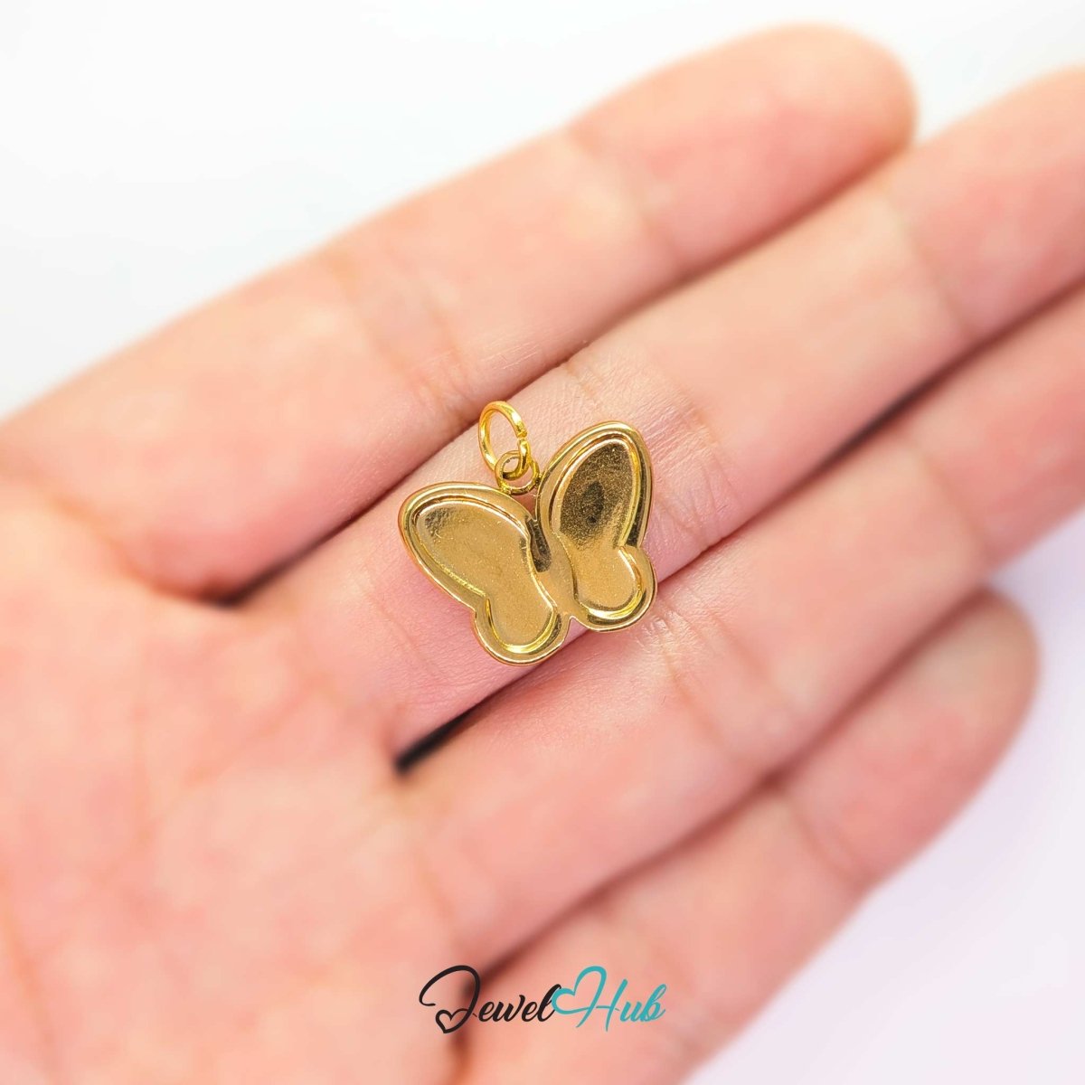 Gold butterfly charm held on a fingertip to show how small the 17mm design really is - JewelHub