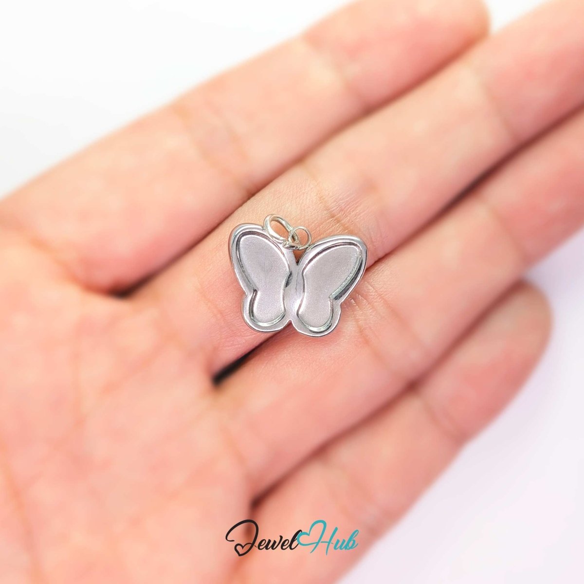 Silver butterfly charm held on a fingertip to show how small the 17mm design really is - JewelHub