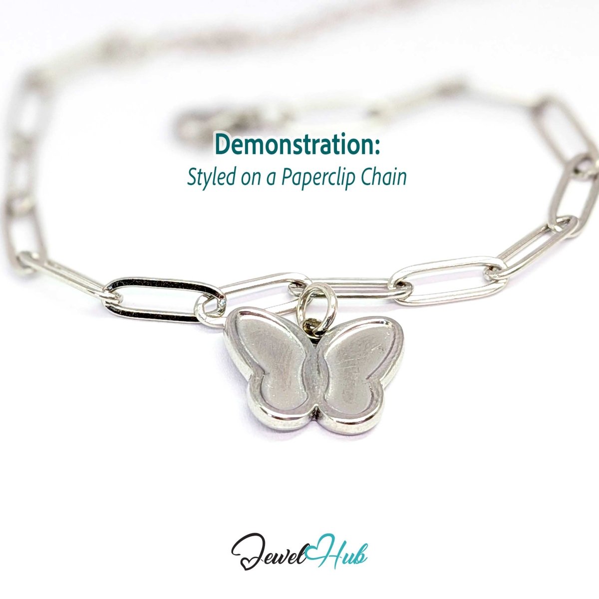 Silver butterfly charm hanging from a silver paperclip chain bracelet - JewelHub