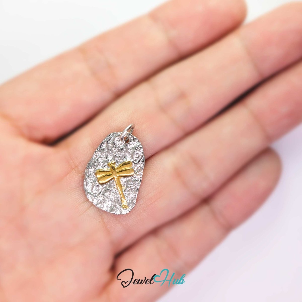 Two-tone dragonfly charm held on a fingertip to show its compact 19mm drop - JewelHub