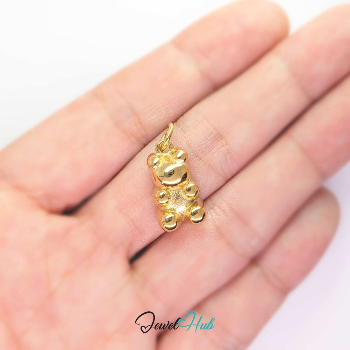 Gold Classic Gummy Bear charm held in the hand to show its size against a fingertip - JewelHub