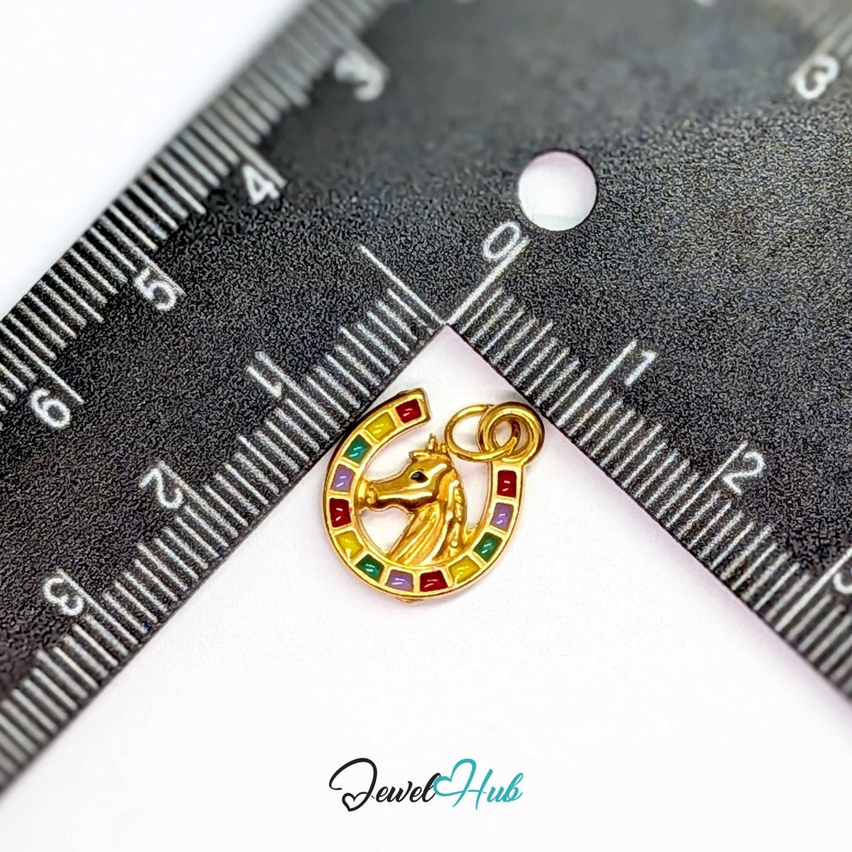 Horseshoe charm in gold stainless steel with a horse head and enamel - beside a ruler for scale - JewelHub