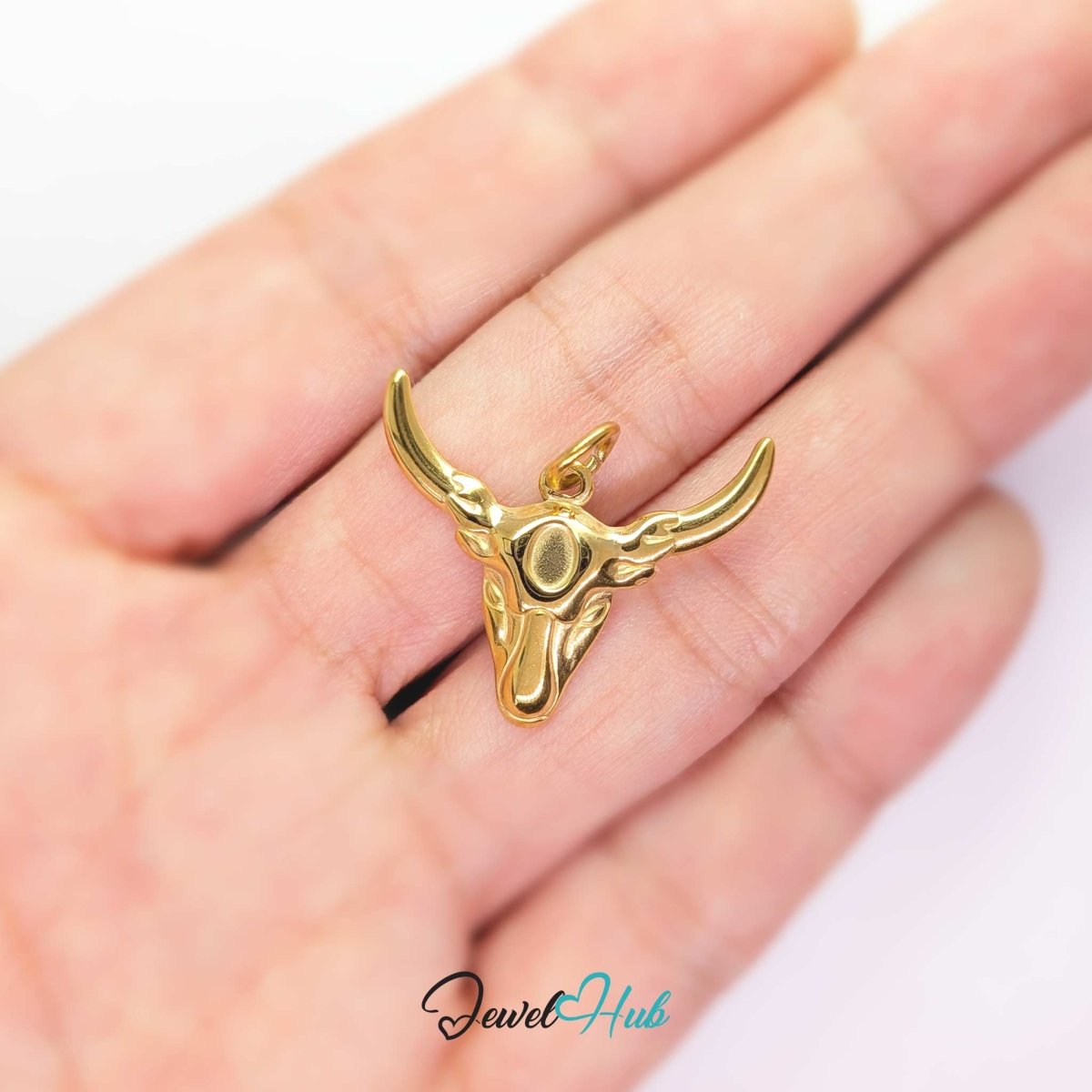 Gold longhorn bull charm held in the hand to show its width against the fingers - JewelHub
