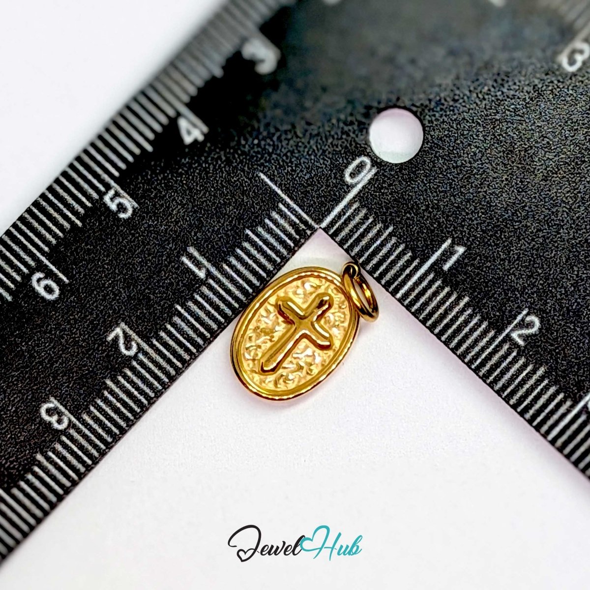 Oval cross medallion charm in gold stainless steel - beside a ruler for scale - JewelHub