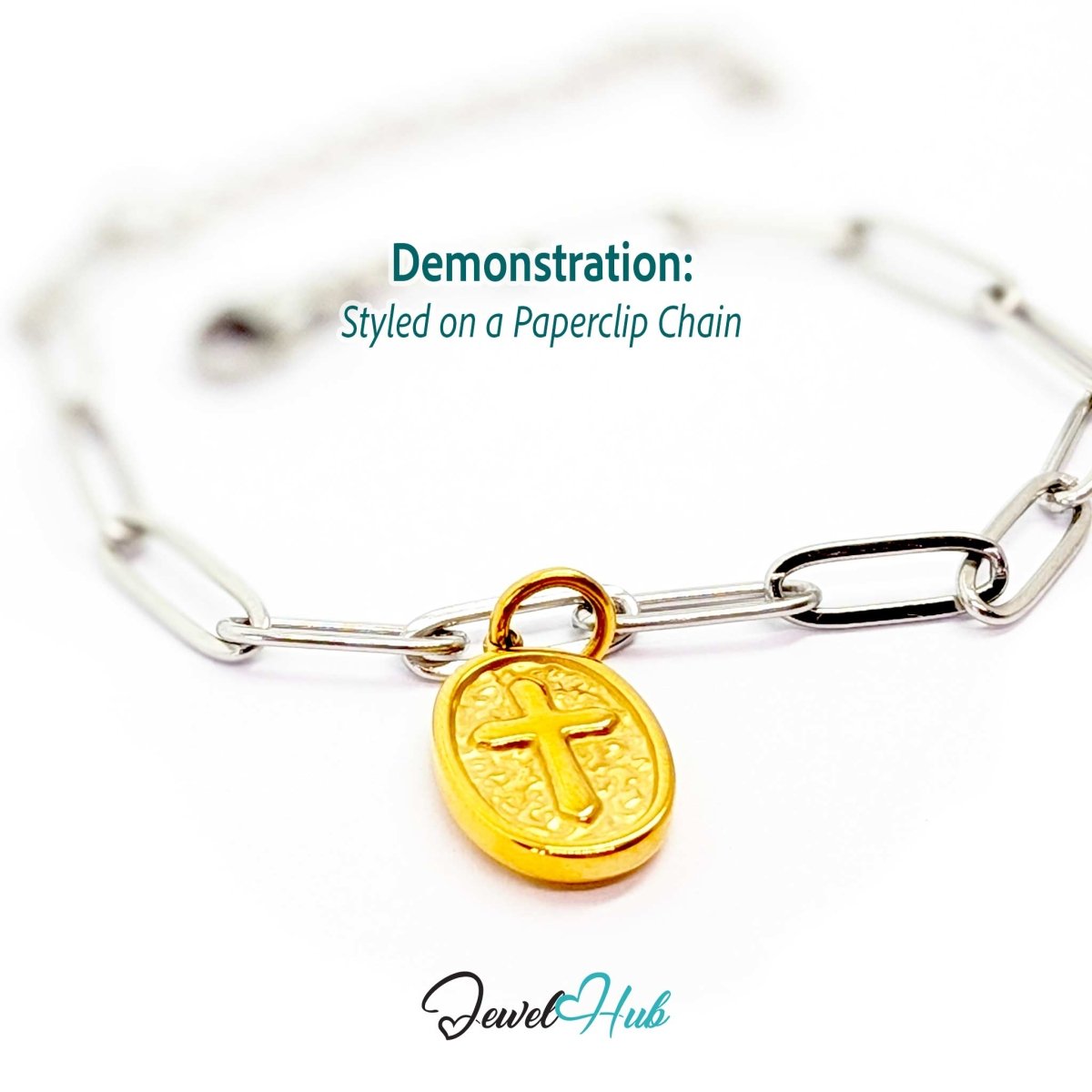 Oval cross medallion charm in gold stainless steel - styled on a silver paperclip chain bracelet - JewelHub
