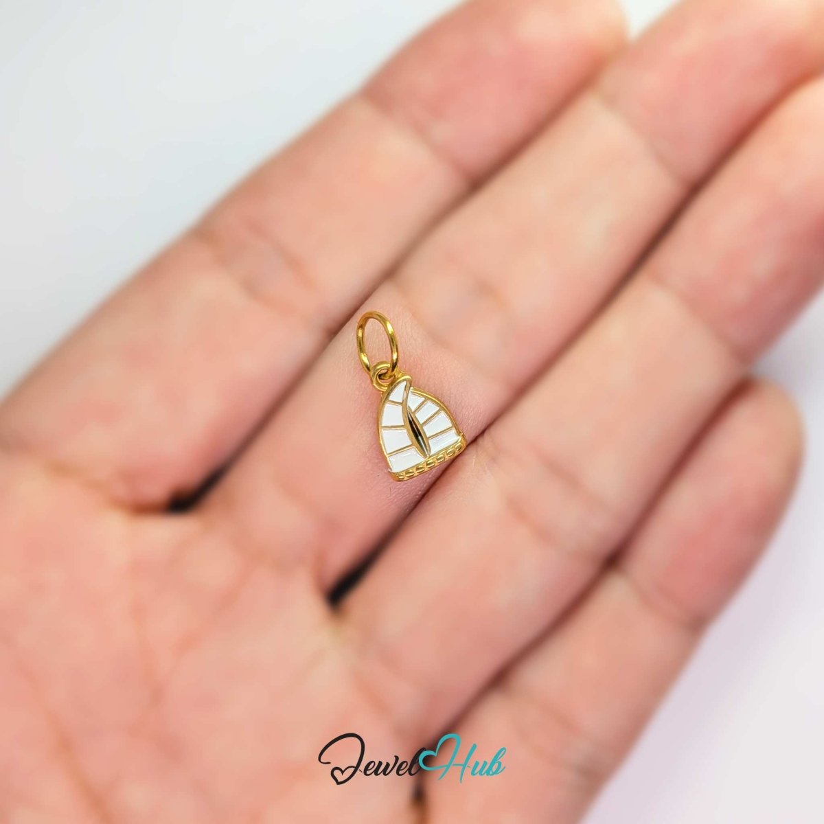 Sailboat charm in gold stainless steel with an openwork sail - held in the hand for scale - JewelHub