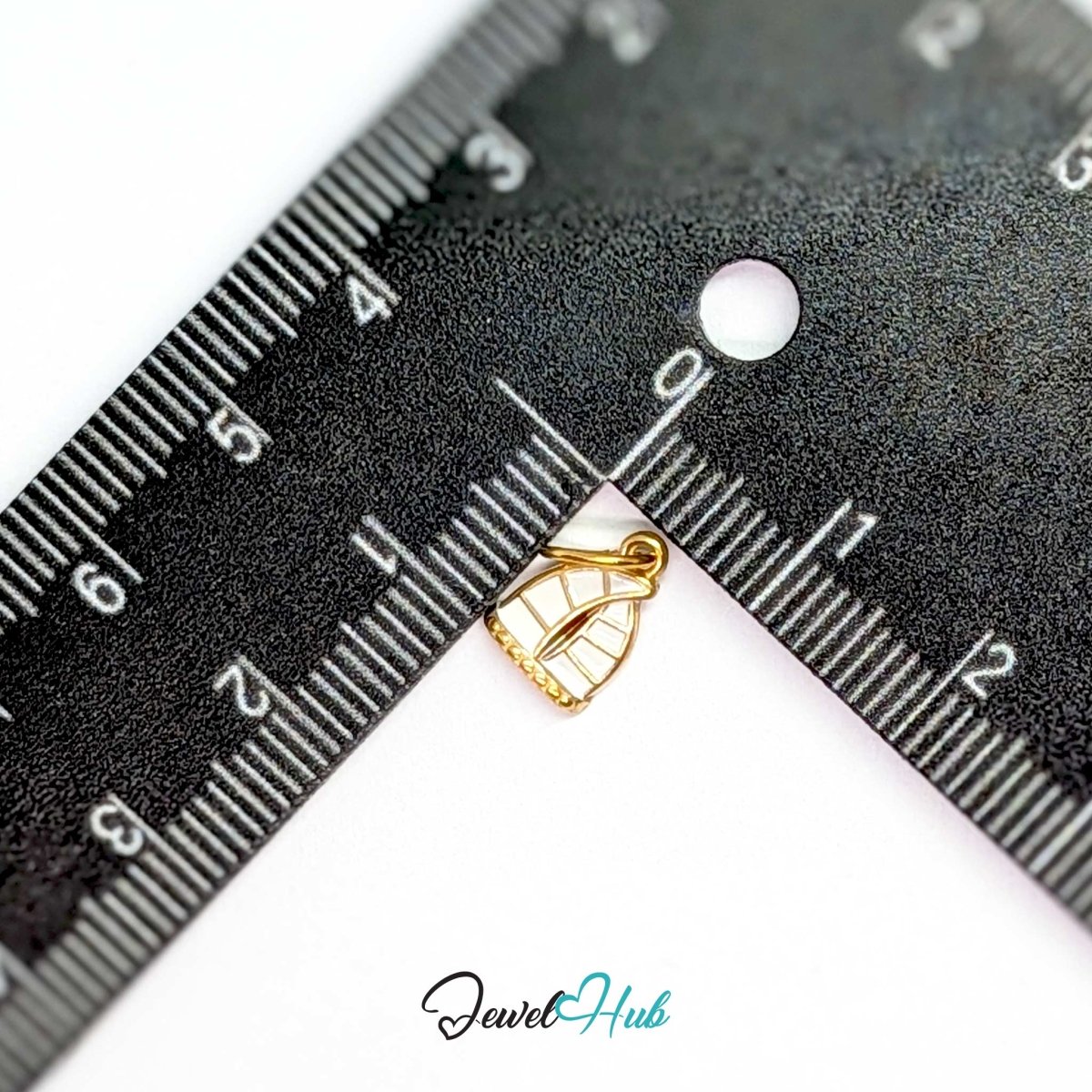 Sailboat charm in gold stainless steel with an openwork sail - beside a ruler for scale - JewelHub