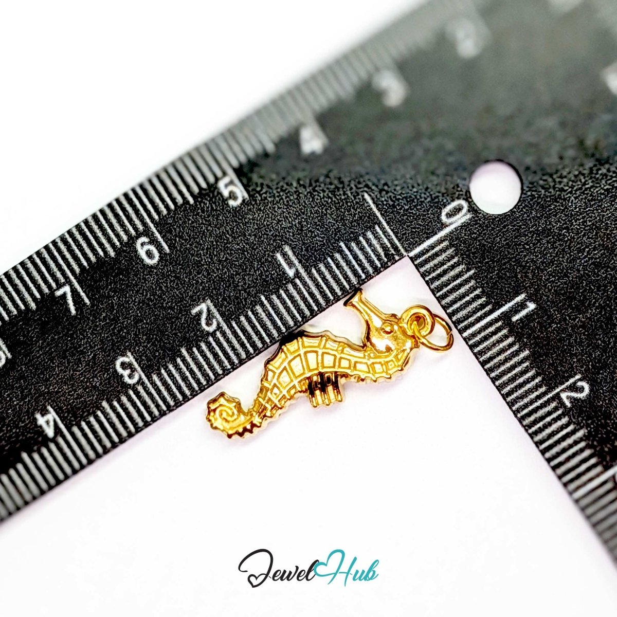 Gold seahorse charm measured against a ruler at 26.4mm tall by 8.6mm wide - JewelHub