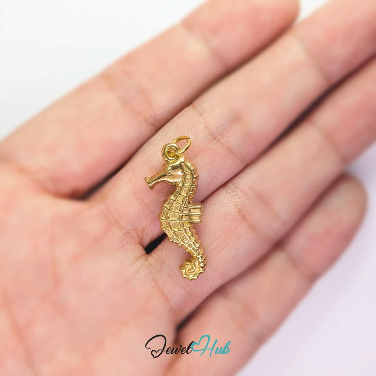 Gold seahorse charm held in the hand to show its size against a fingertip - JewelHub