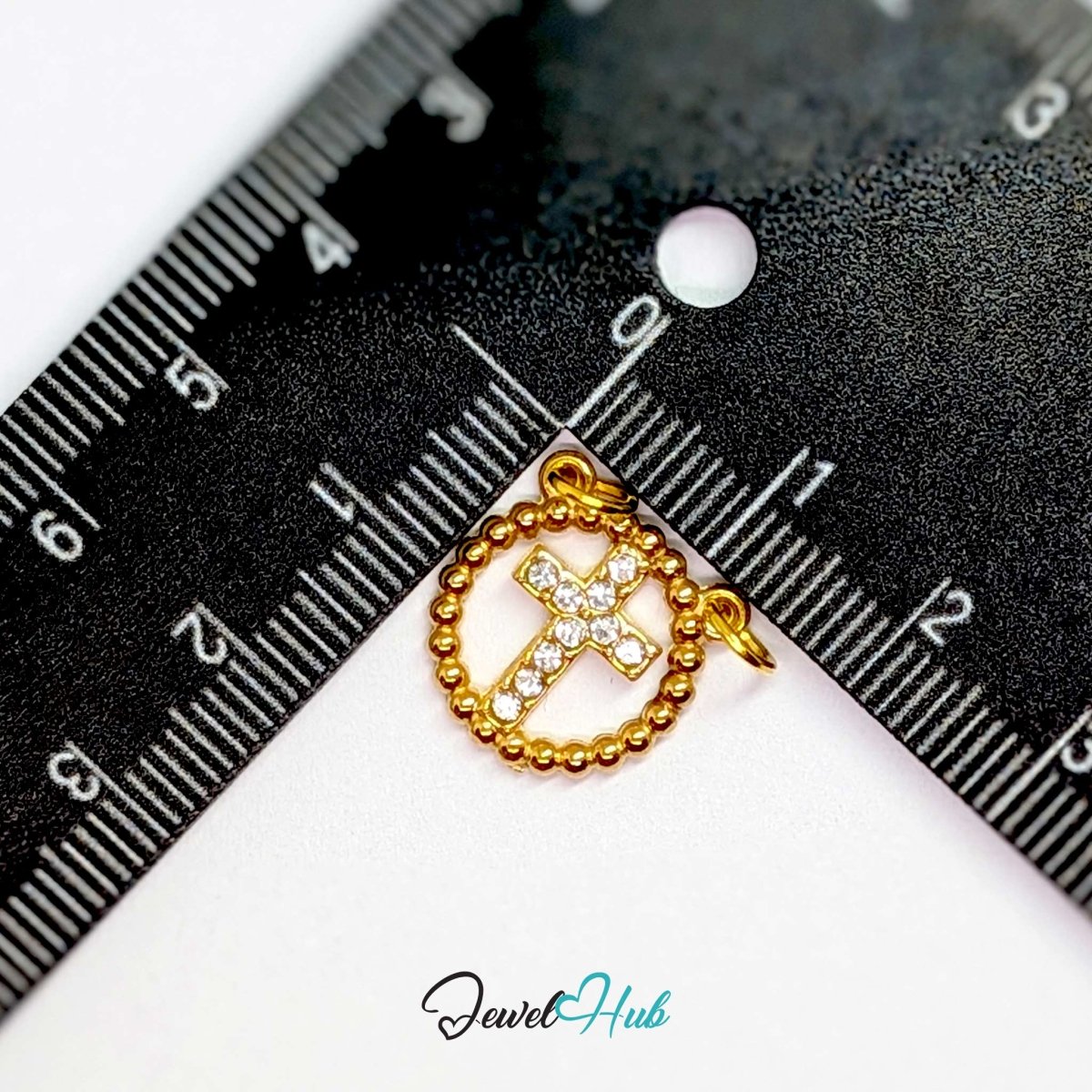 Cross charm in gold stainless steel with ten crystals in a beaded ring - beside a ruler for scale - JewelHub