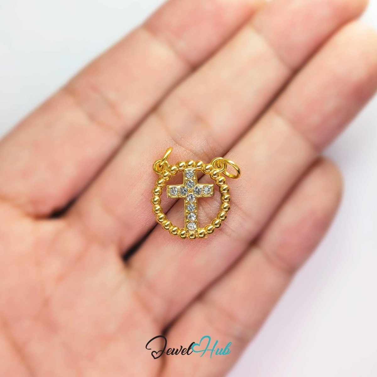 Cross charm in gold stainless steel with ten crystals in a beaded ring - held in the hand for scale - JewelHub