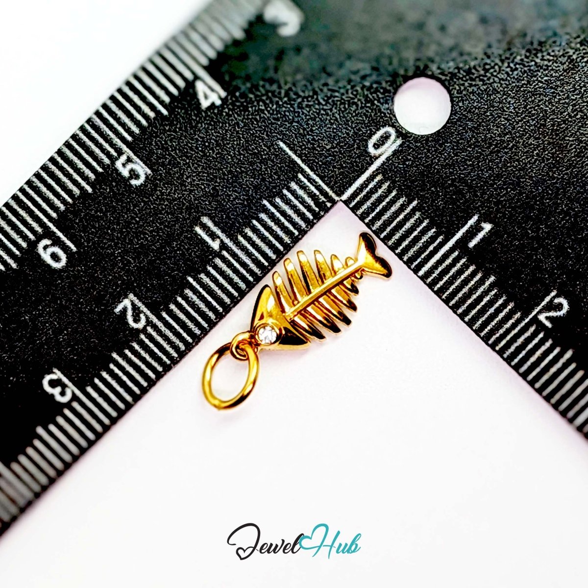 Fish bone charm in gold stainless steel with a crystal eye - beside a ruler for scale - JewelHub