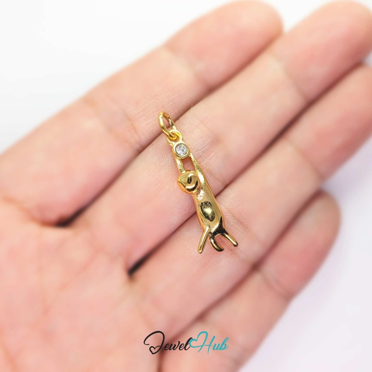 Gold hanging cat charm held in the hand to show its long narrow drop - JewelHub