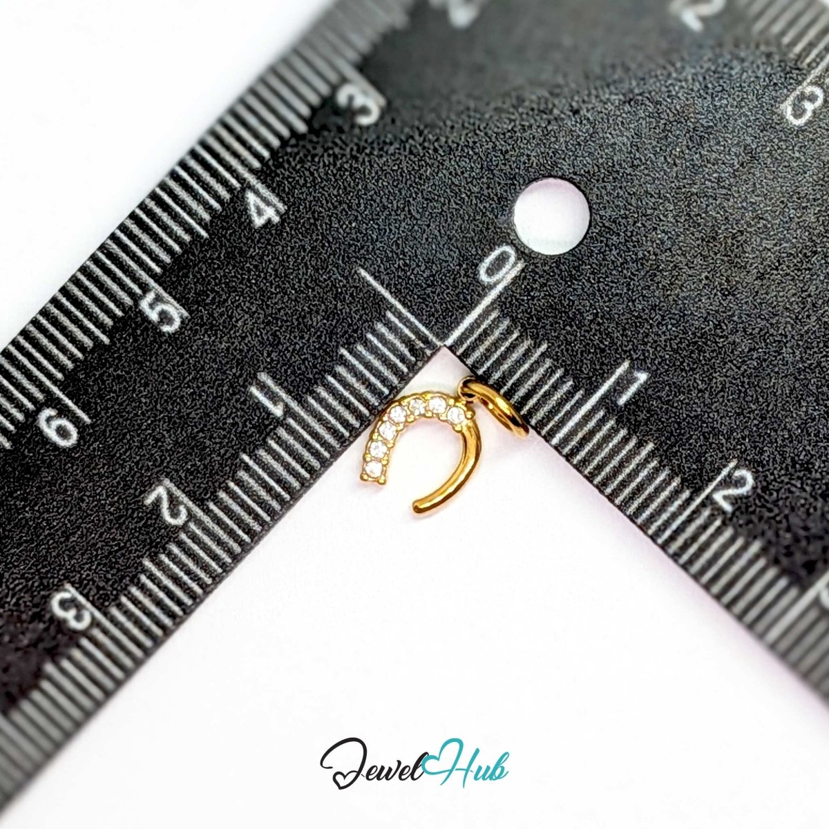 Mini horseshoe charm in gold stainless steel with seven crystals - beside a ruler for scale - JewelHub