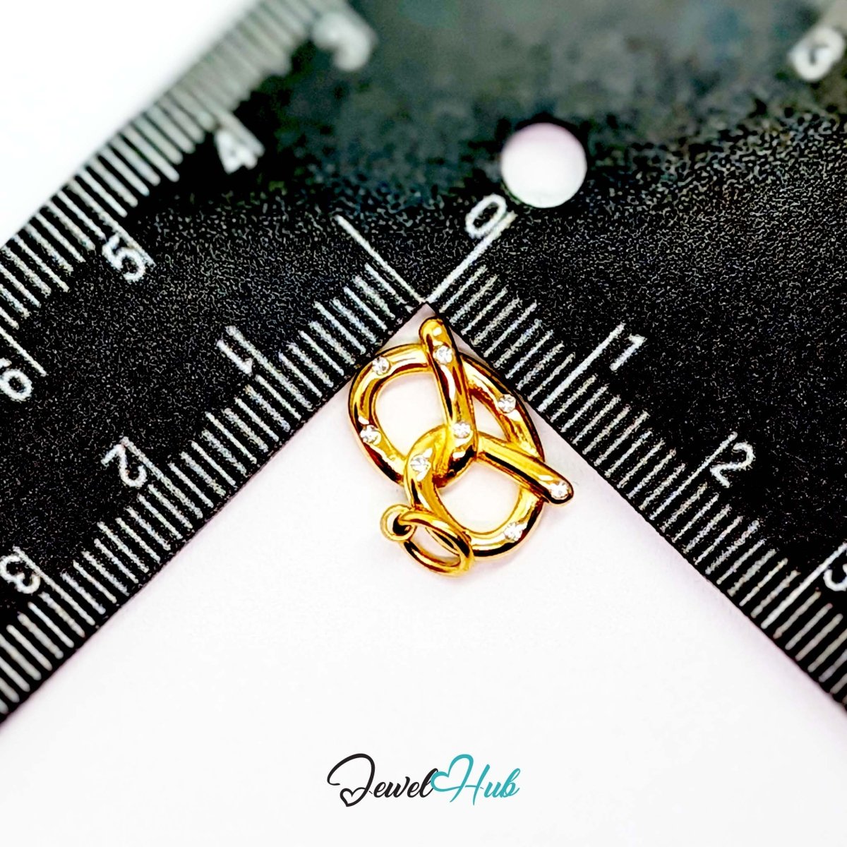 Pretzel charm in gold stainless steel with clear crystals - beside a ruler for scale - JewelHub
