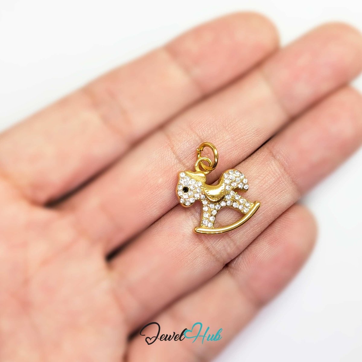 Gold Crystal Rocking Horse charm held in the hand to show its size against a fingertip - JewelHub