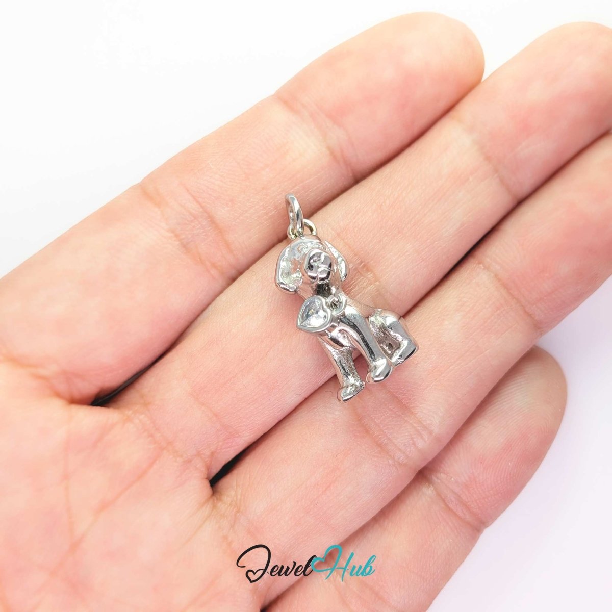 Silver sitting puppy charm held in the hand to show its size against a fingertip - JewelHub