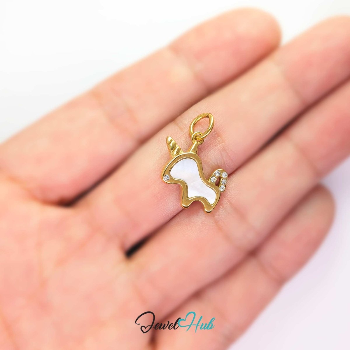 Gold unicorn charm held on a fingertip to show how small the 17mm design really is - JewelHub