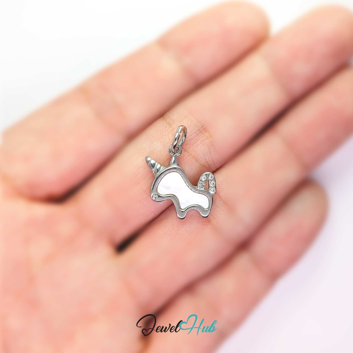 Silver unicorn charm held on a fingertip to show how small the 17mm design really is - JewelHub