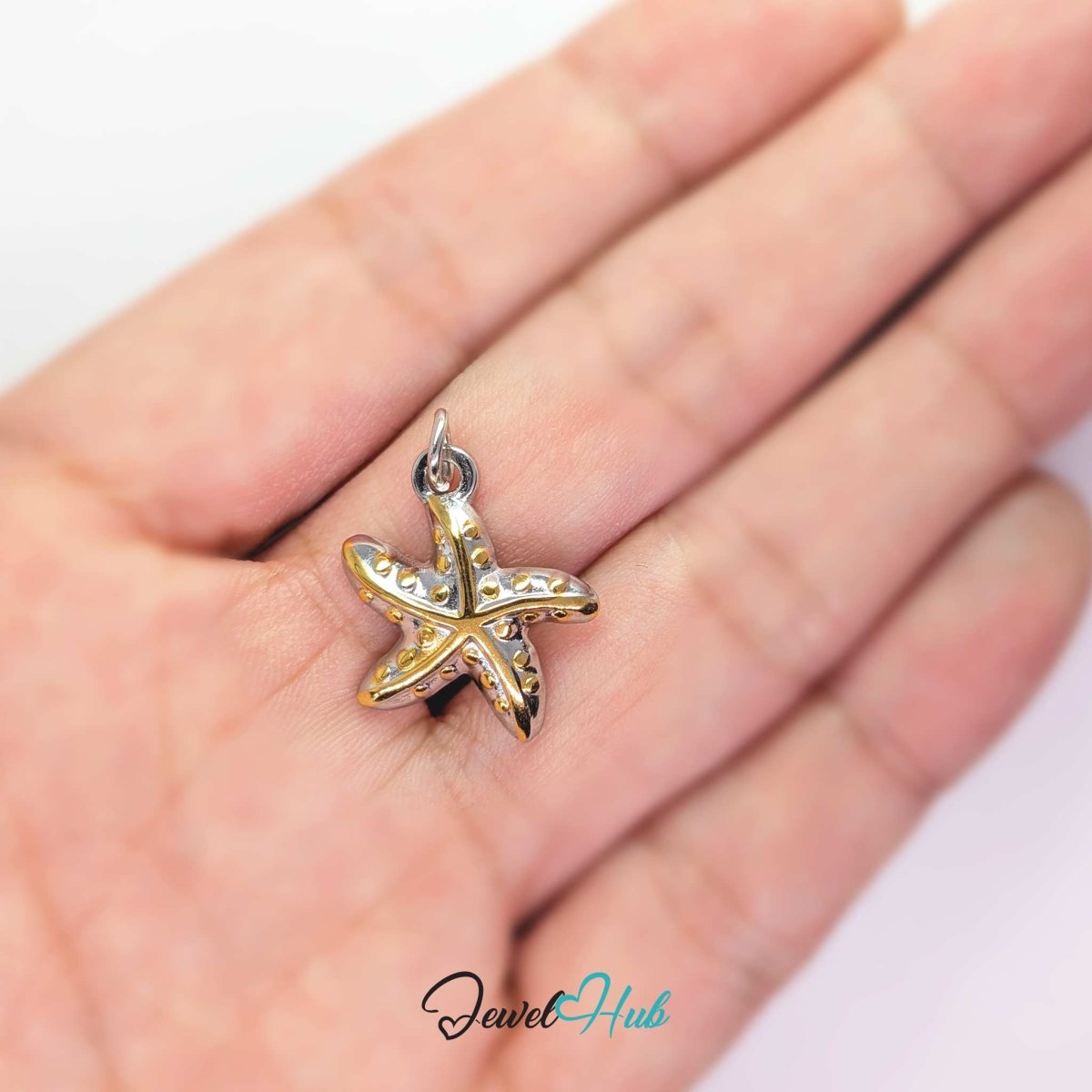 DuoTone starfish charm held in the hand to show its size against a fingertip - JewelHub