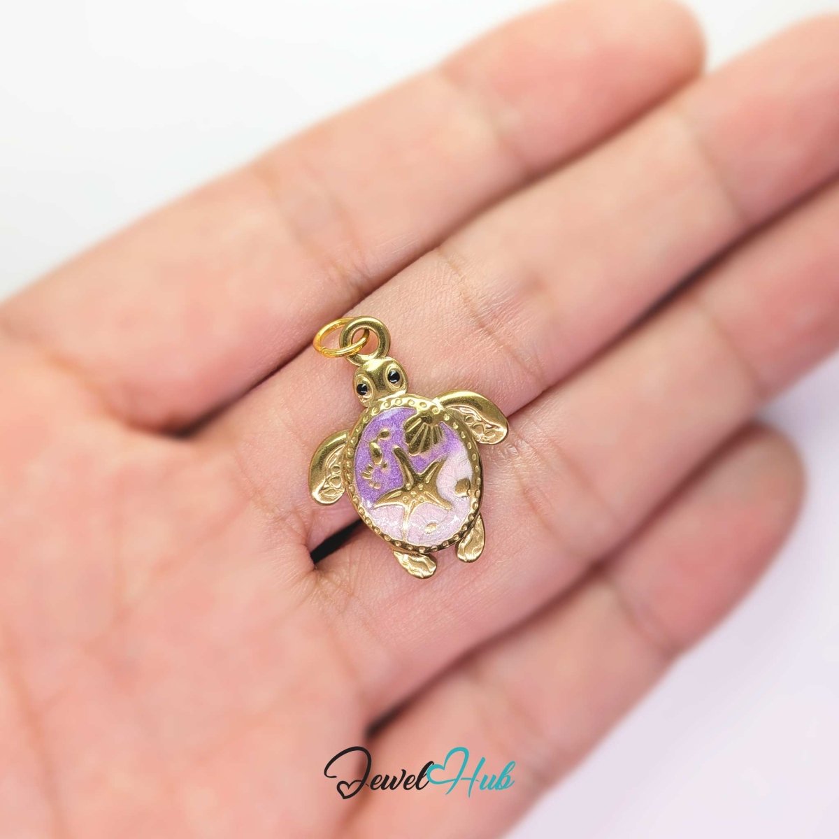 Purple enamel sea turtle charm held in the hand to show its size against a fingertip - JewelHub