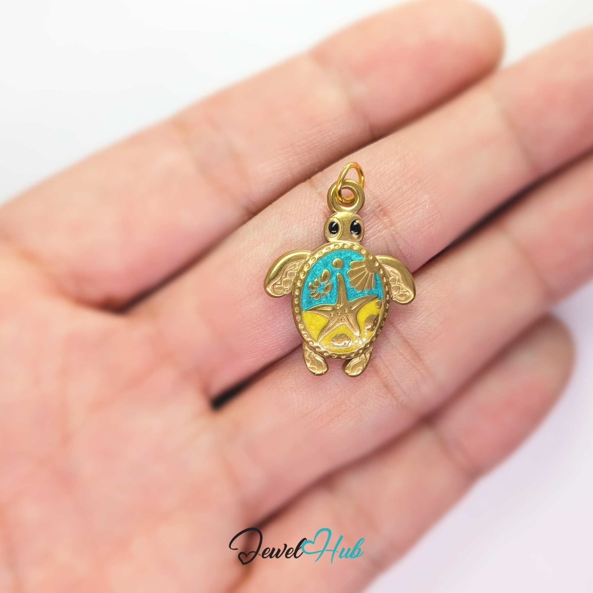 Turquoise enamel sea turtle charm held in the hand to show its size against a fingertip - JewelHub