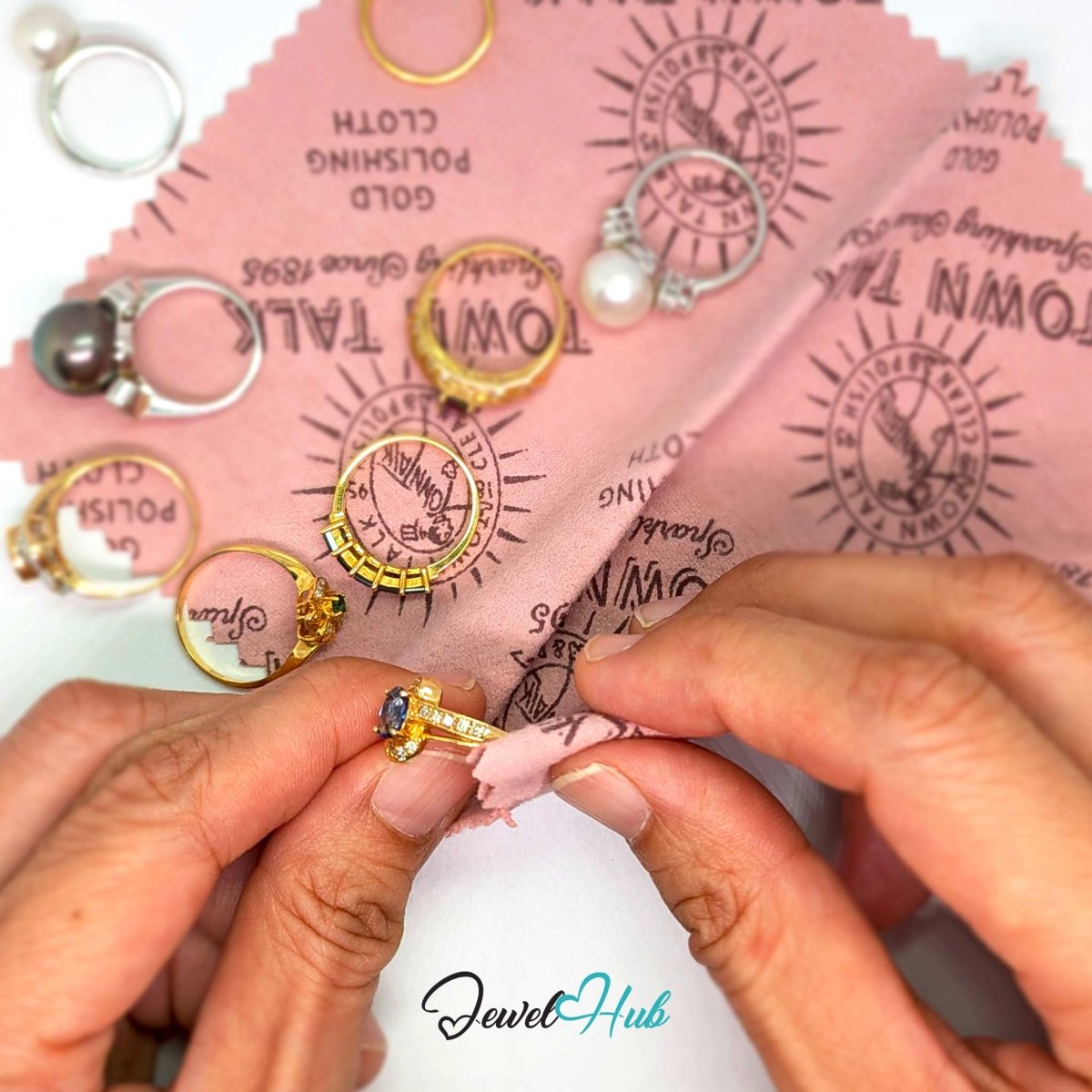 Polishing a gold gemstone ring by hand with the Town Talk cloth, surrounded by gold rings and a pearl ring on a white background.