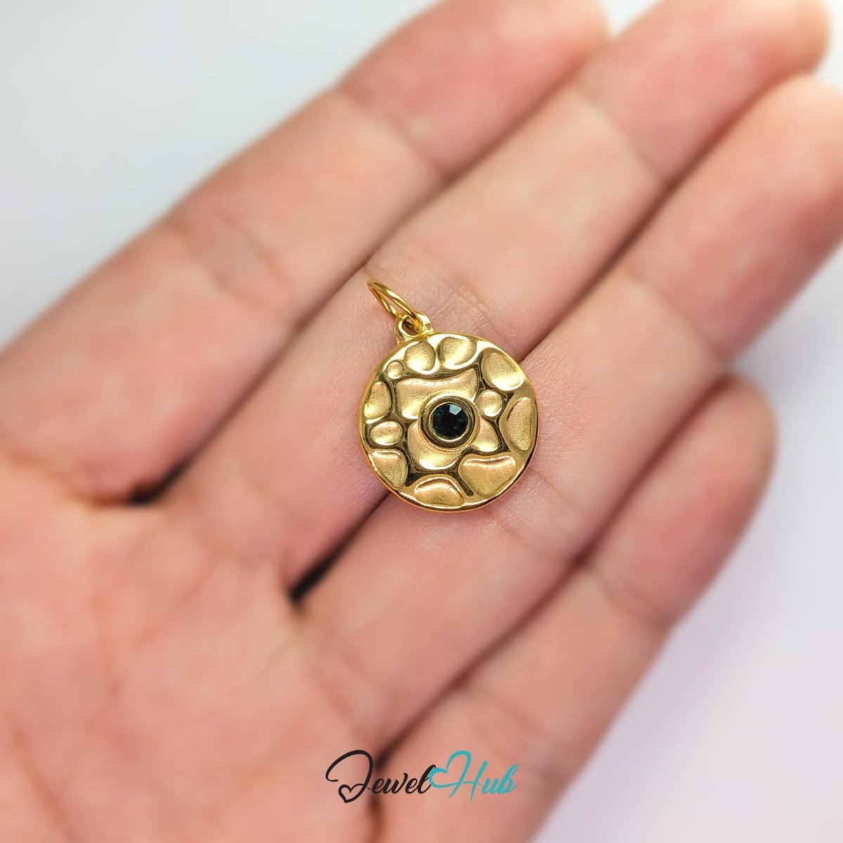 Hammered disc charm in gold stainless steel with a green stone - held in the hand for scale - JewelHub