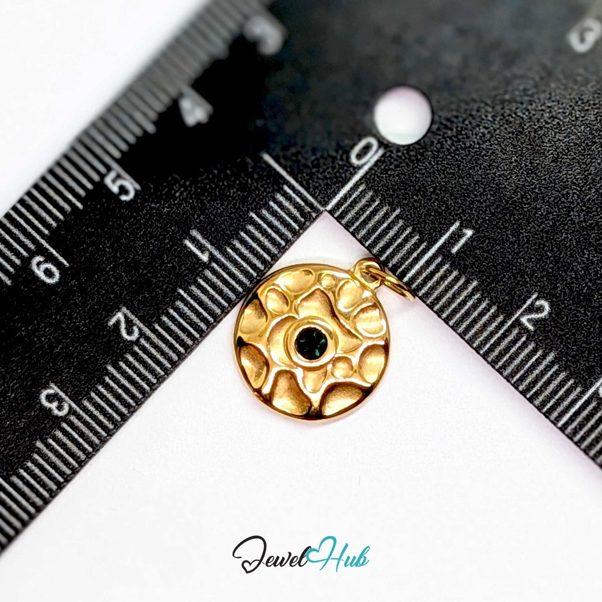 Hammered disc charm in gold stainless steel with a green stone - beside a ruler for scale - JewelHub