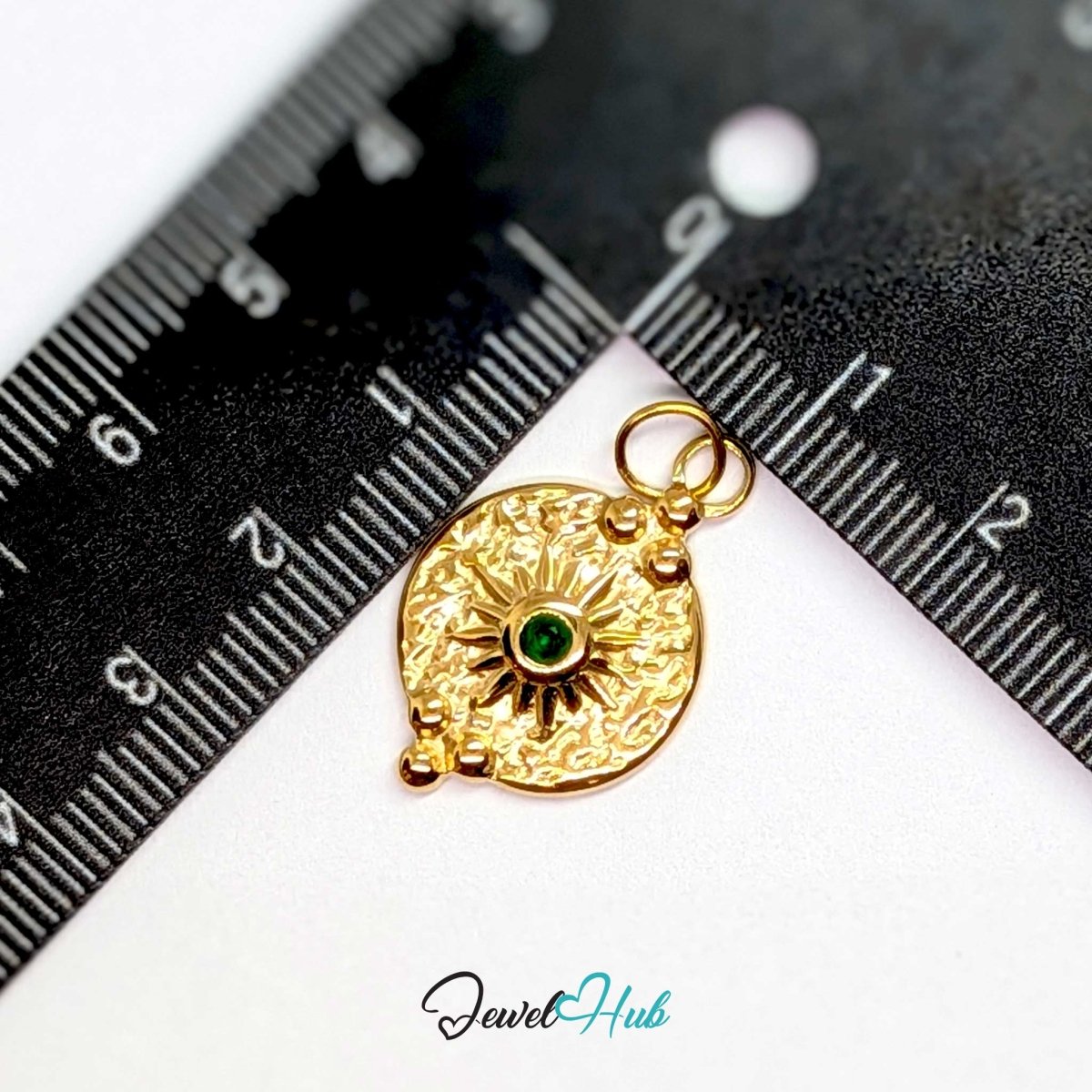 Rosette medallion charm in gold stainless steel with a green gem - beside a ruler for scale - JewelHub