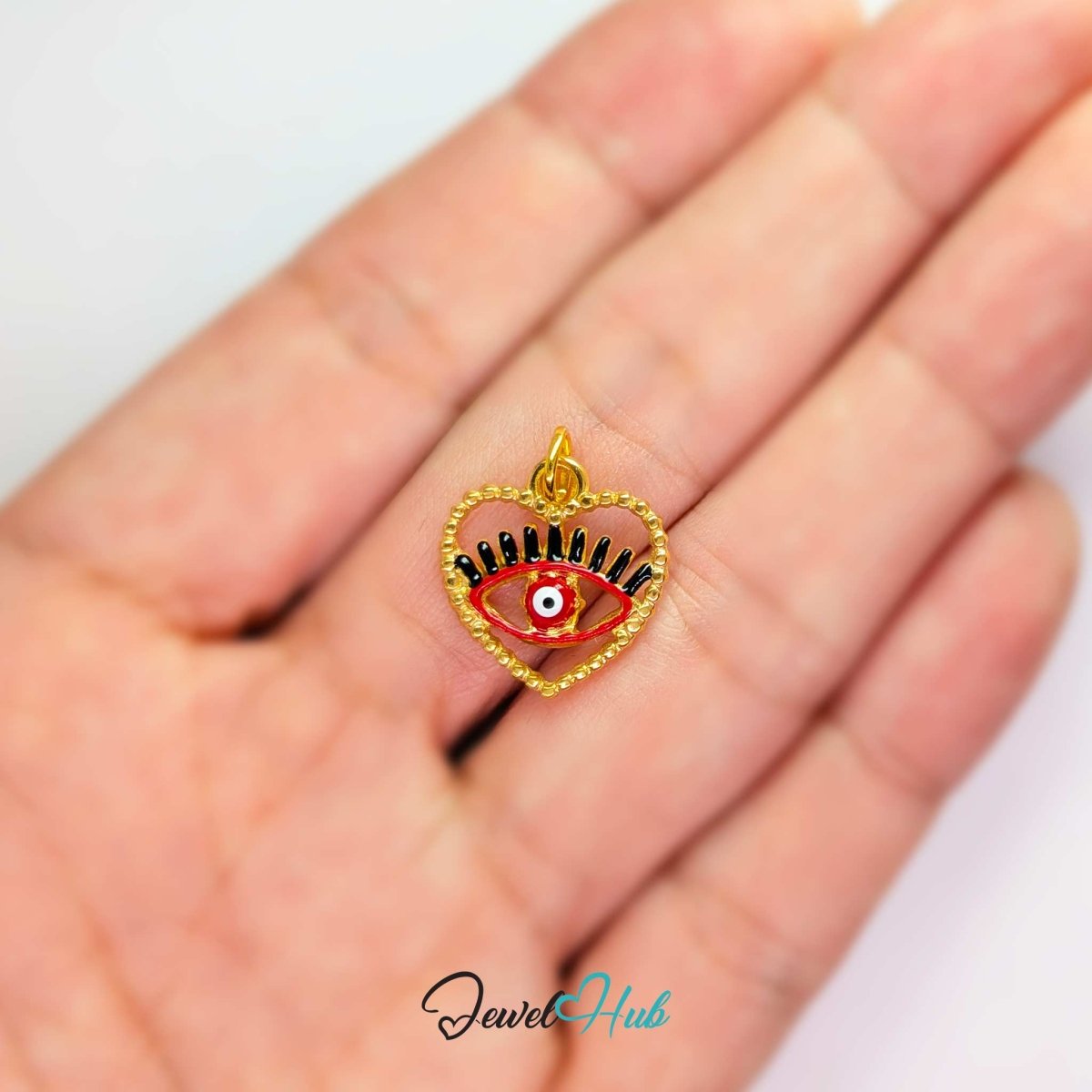Red Hollow Evil Eye charm, gold stainless steel with enamel, held in the hand to show its size - JewelHub