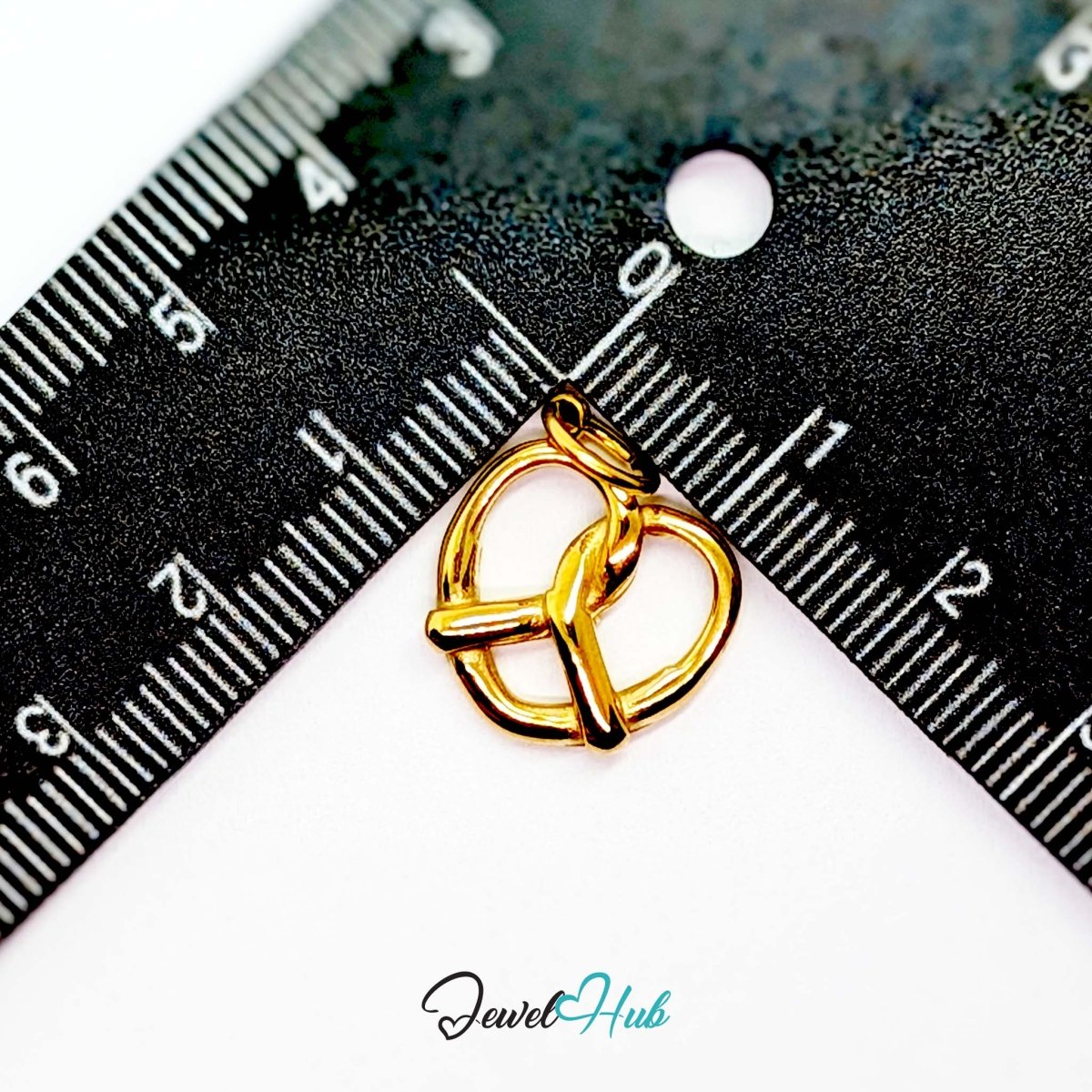 Large openwork pretzel charm in gold stainless steel - beside a ruler for scale - JewelHub