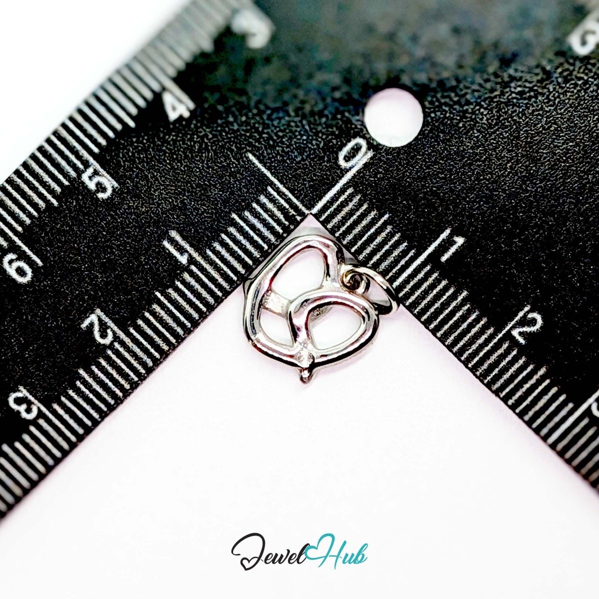 Openwork pretzel charm in silver stainless steel - beside a ruler for scale - JewelHub