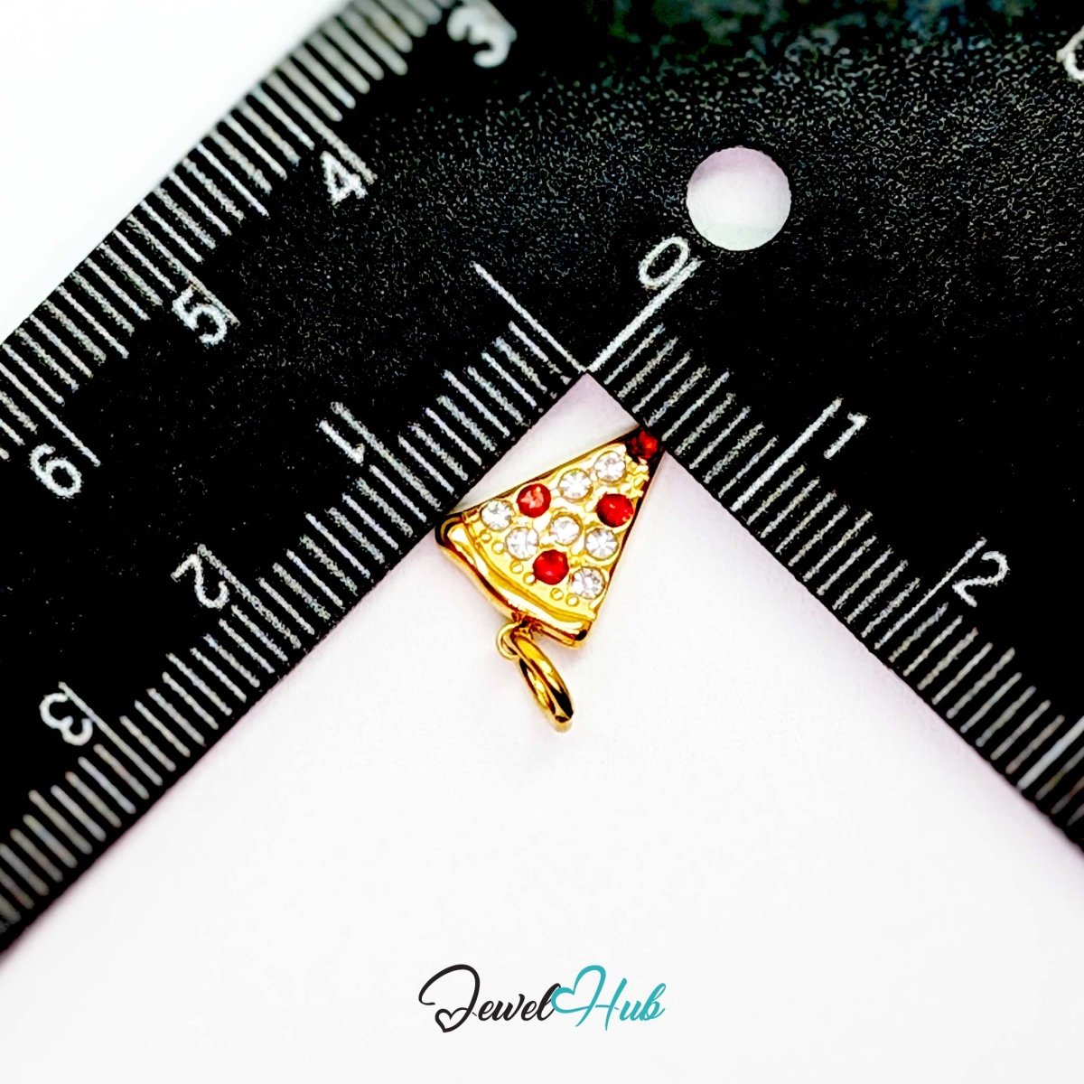 Pizza slice charm in gold stainless steel set with clear and red crystals - beside a ruler for scale - JewelHub