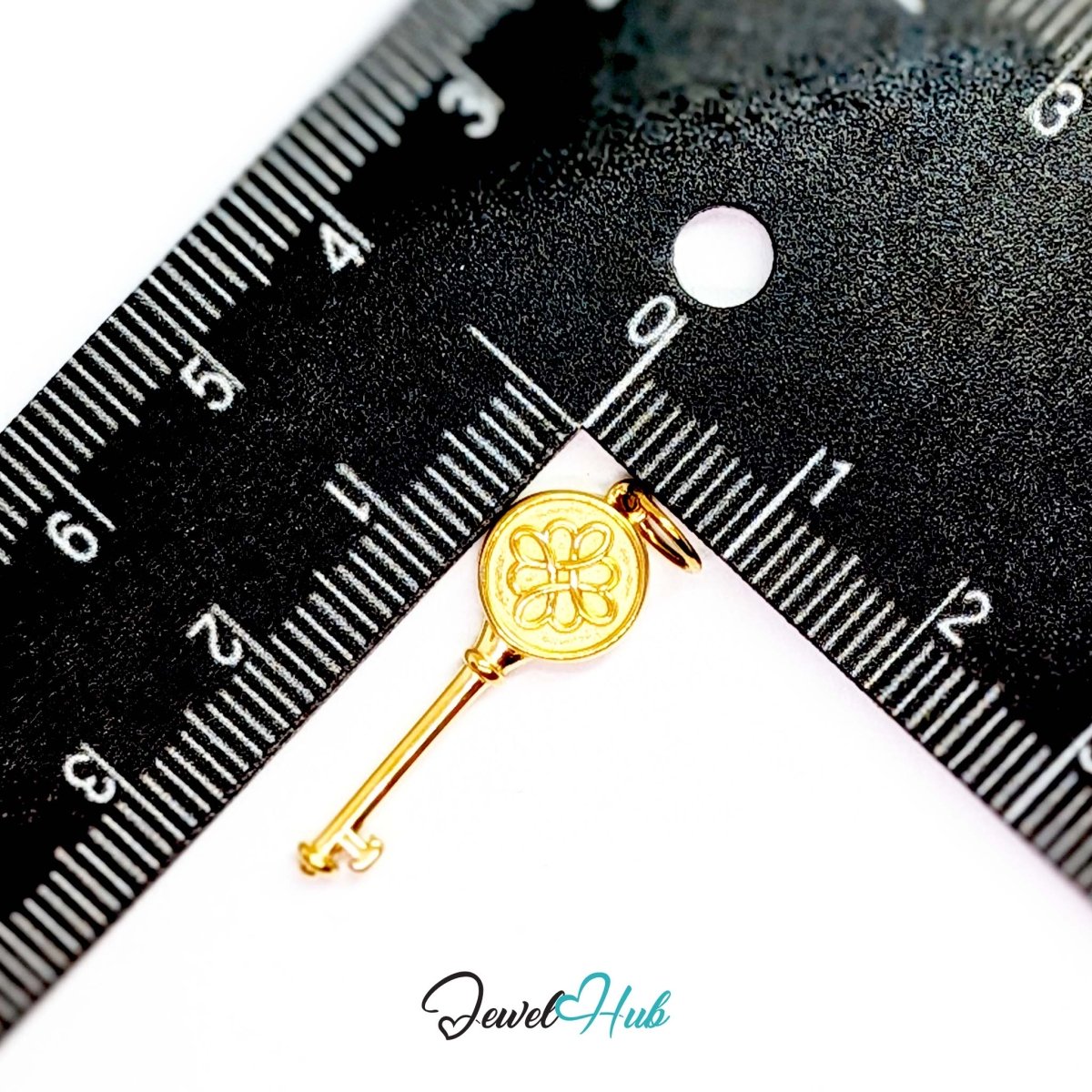 Round openwork key charm in gold stainless steel - beside a ruler for scale - JewelHub