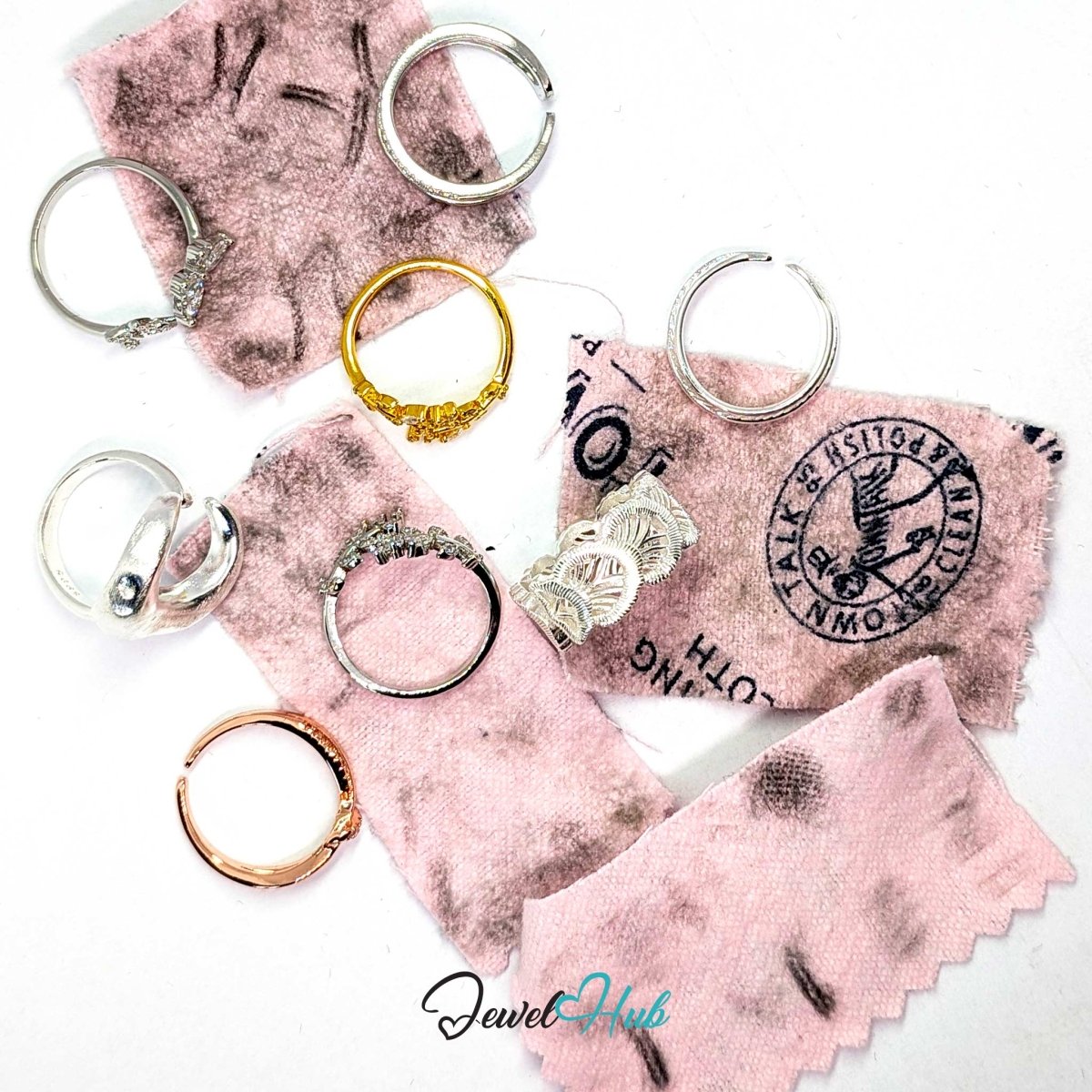 Several silver-toned rings with textured, engraved, and filigree details are arranged on pink fabric swatches with black stamp-like markings on a white background. A 'JewelHub' watermark is visible at the bottom.