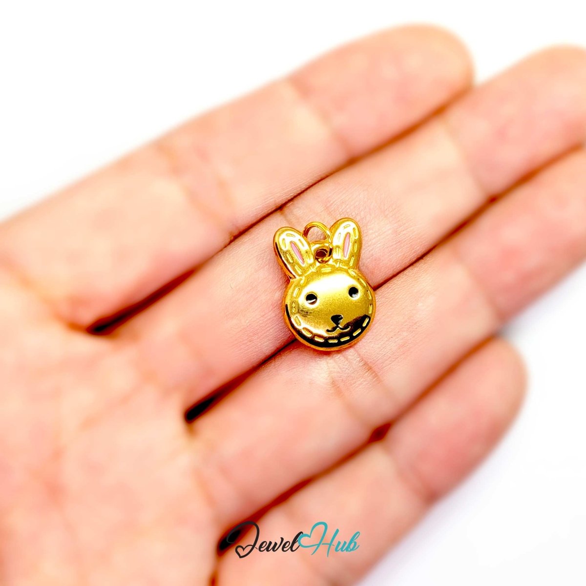 Gold Stitched Bunny Head charm held in the hand to show its size against a fingertip - JewelHub